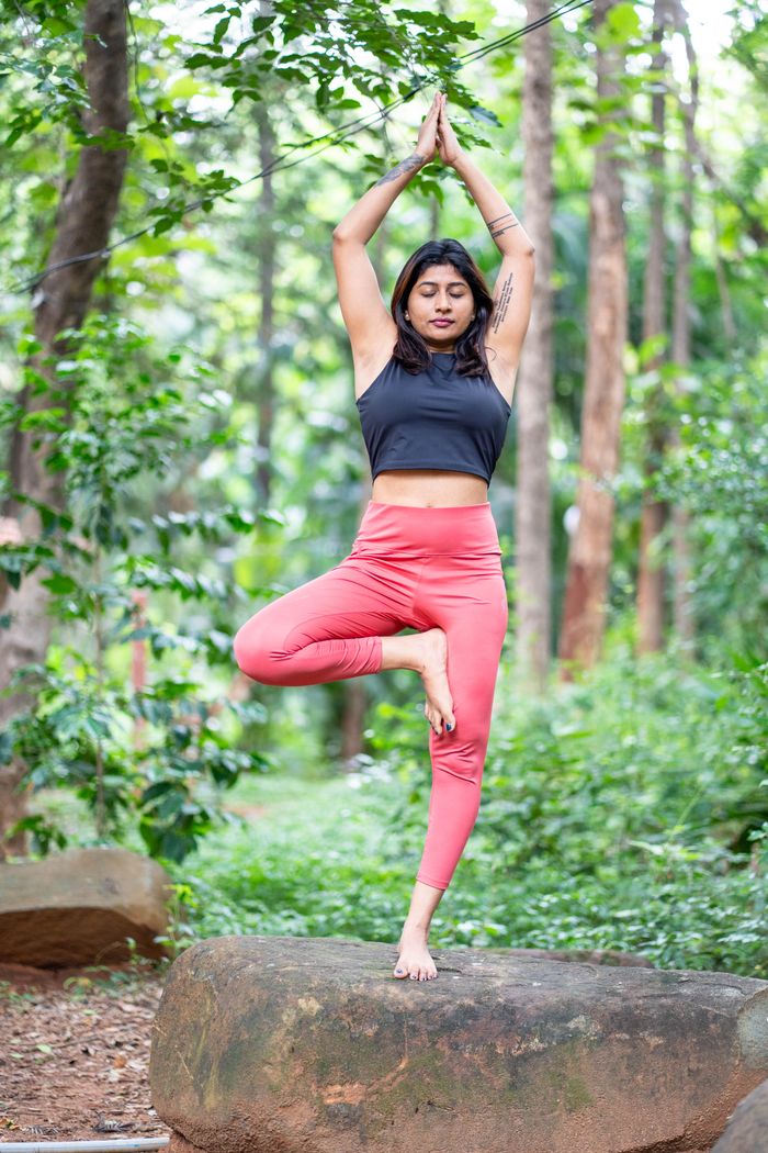 services-03 Female doing yoga tree pose on a rock in a lush forest setting, promoting mindfulness and fitness.