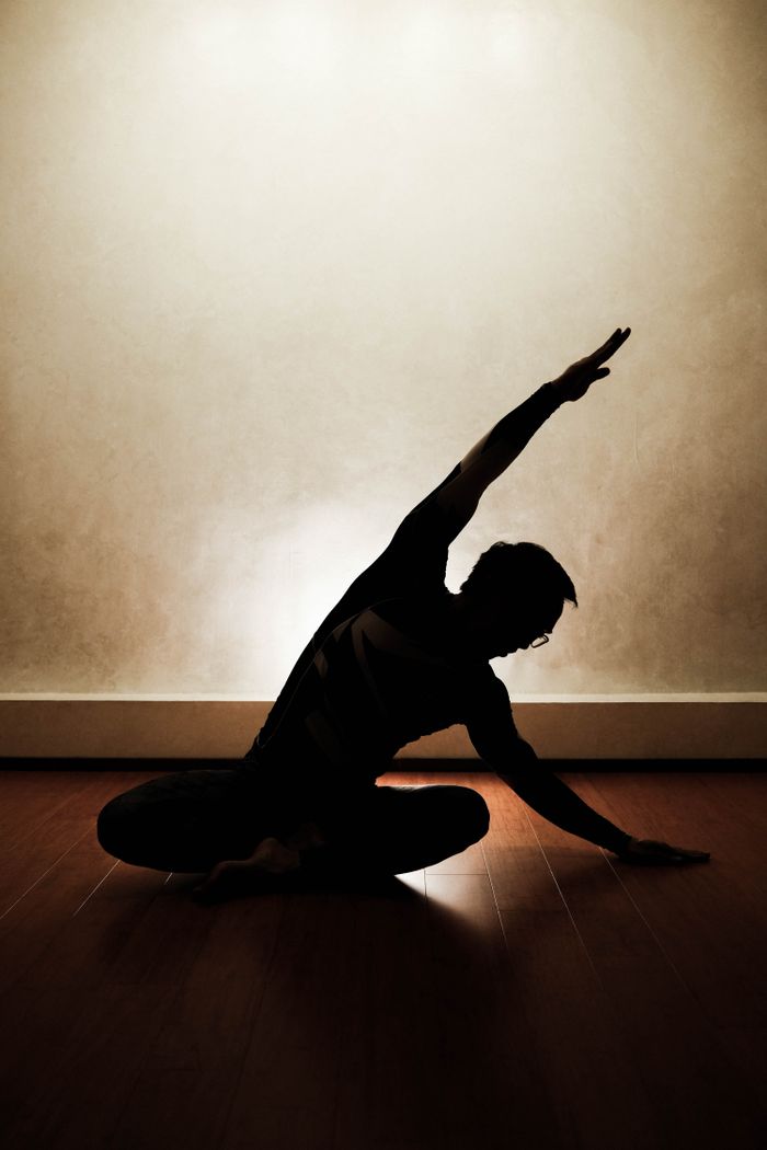 who-we-are Silhouette of a person performing a yoga pose indoors with dramatic lighting.